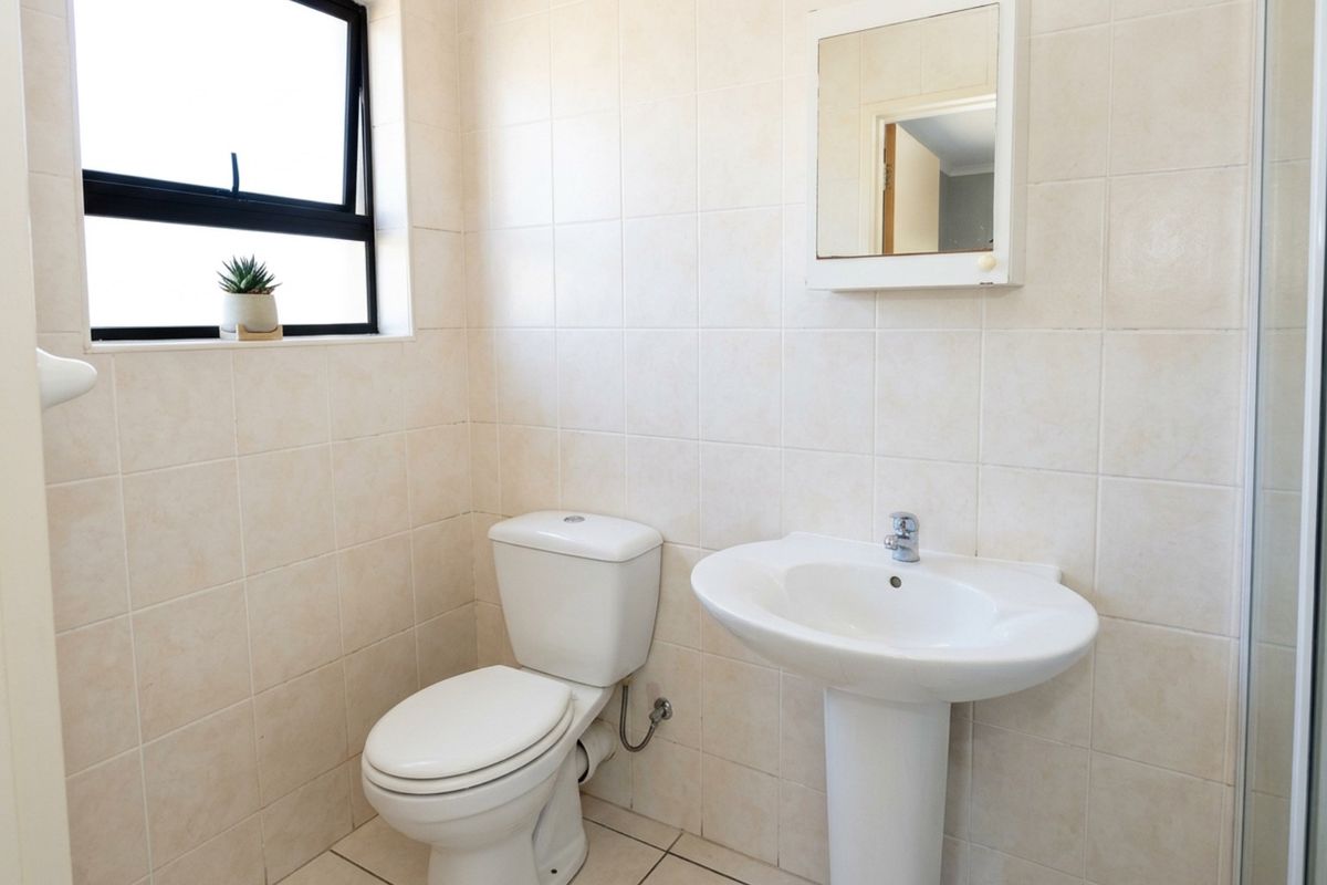 A functional bathroom featuring a pedestal sink, a standard toilet, and wall-to-wall tiling with a window for natural light.