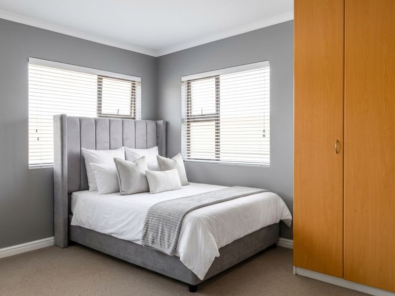 A well-maintained bedroom featuring neutral grey walls, carpeted flooring, and built-in wooden cabinetry.
