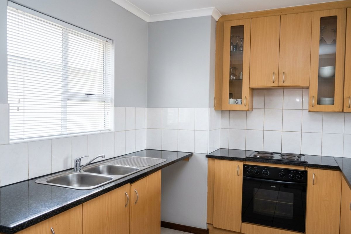 Functional kitchen featuring light wood cabinetry, dark countertops, a built-in oven with hob, and a double stainless steel sink.