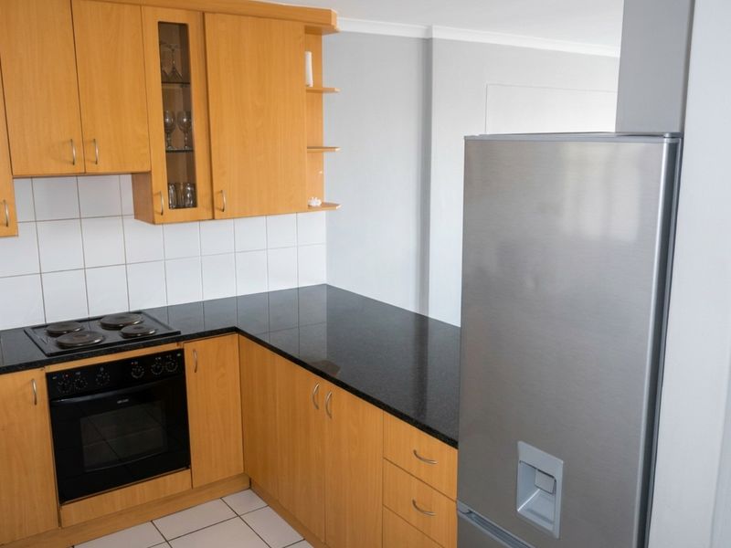 A functional kitchen featuring light wood cabinetry, dark granite countertops, a built-in oven, and a ceramic hob with a tiled backsplash.