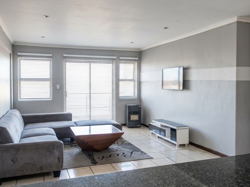 A bright living room featuring tiled flooring, recessed ceiling lighting, and large windows with fitted blinds, offering a clean and functional living space.