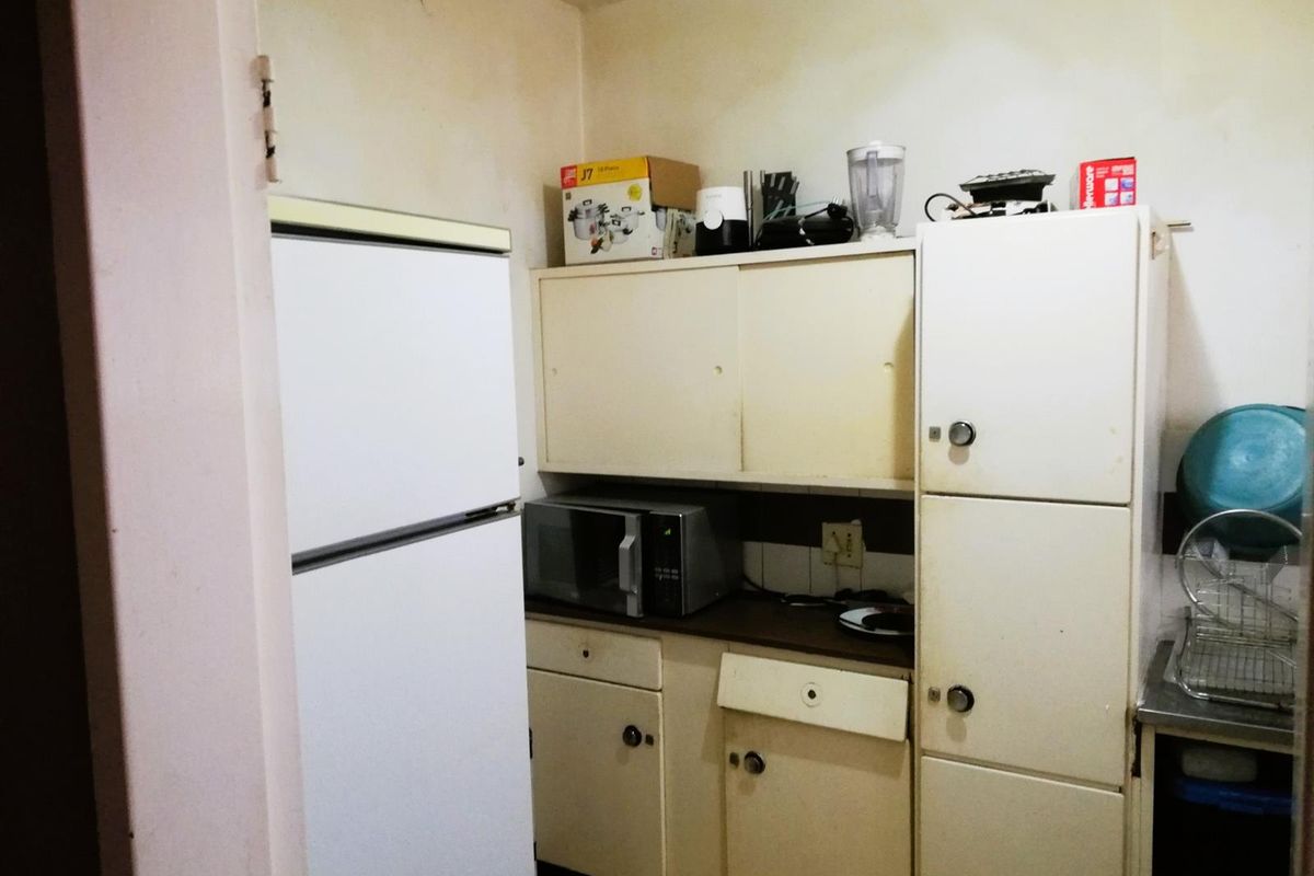 A compact kitchen featuring dated built-in cabinetry, laminate countertops, and a stainless steel sink, requiring cosmetic updates to modernize the space.
