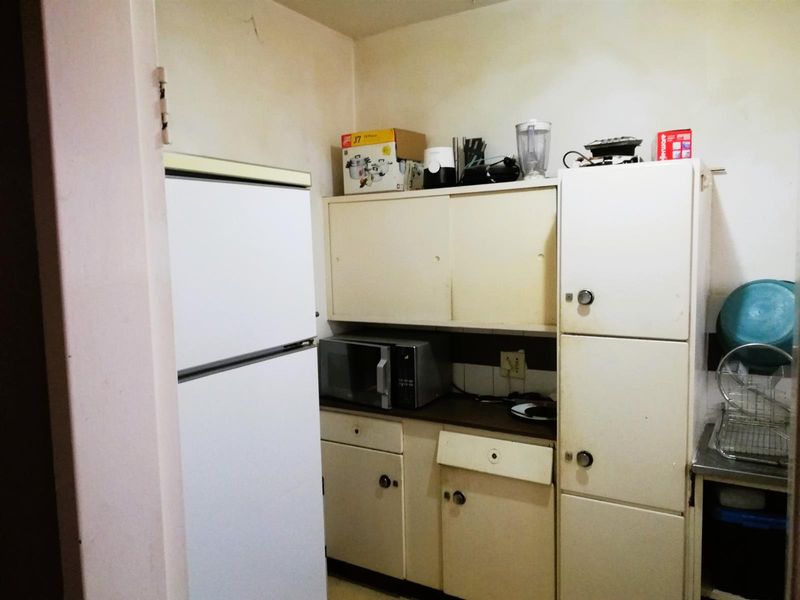 A compact kitchen featuring dated built-in cabinetry, laminate countertops, and a stainless steel sink, requiring cosmetic updates to modernize the space.