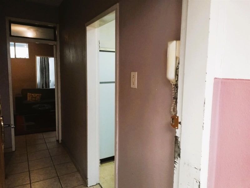 A narrow apartment hallway featuring tiled flooring and a wall-mounted intercom system, leading into adjacent living and kitchen areas.