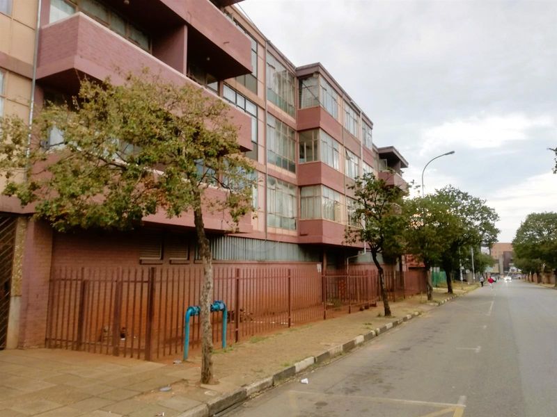 Street view of a multi-story apartment building featuring a brick facade, metal security fencing, and multiple balconies along the front elevation.