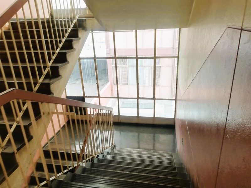 A communal stairwell featuring metal stairs, a metal balustrade, and a large steel-framed window providing natural light to the hallway area.