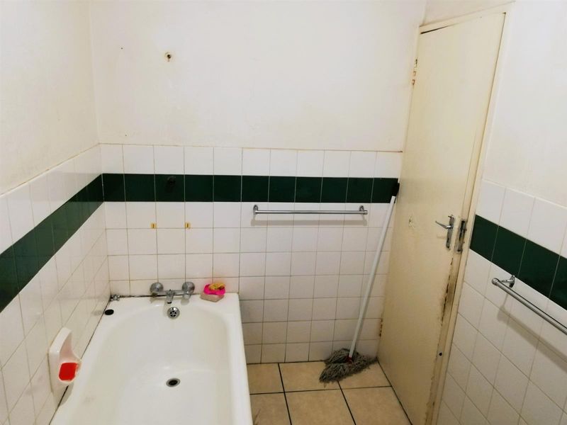 A dated bathroom featuring a standard bathtub, tiled walls with a decorative border, and tiled flooring, requiring cosmetic updates.