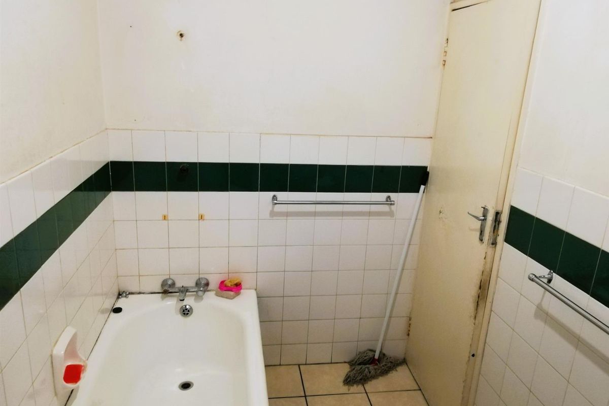A dated bathroom featuring a standard bathtub, tiled walls with a decorative border, and tiled flooring, requiring cosmetic updates.