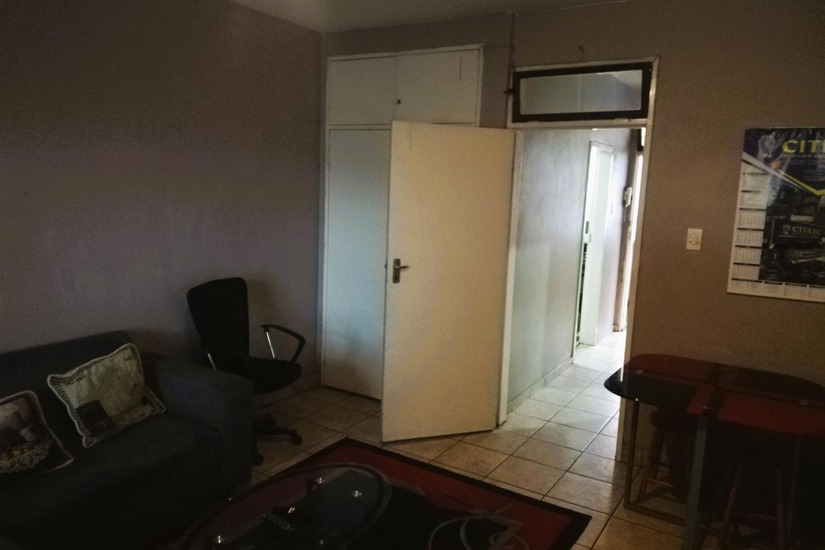 A living area featuring tiled flooring and a built-in cupboard, providing a functional space with direct access to the hallway.