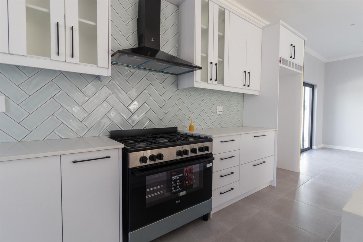 Modern kitchen featuring white cabinetry, herringbone tile backsplash, quartz countertops, and a high-quality freestanding gas stove with an extractor fan.