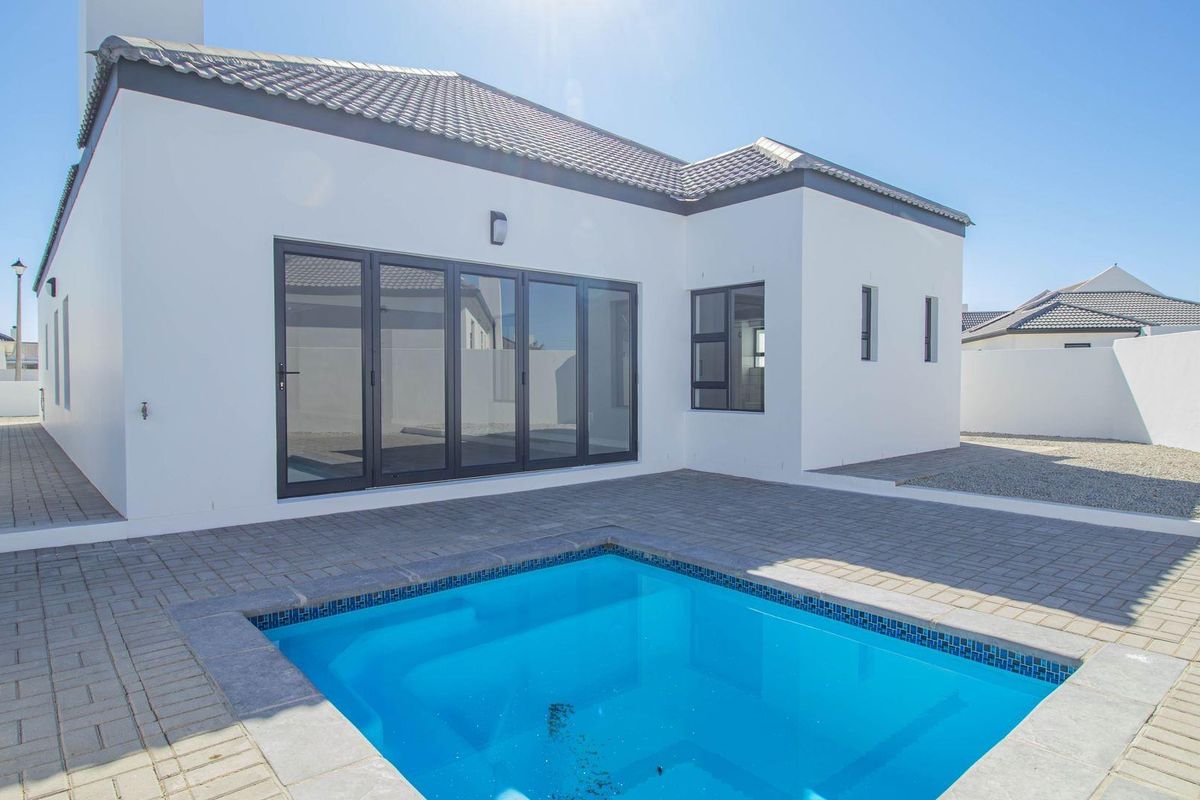 Rear exterior view featuring a modern swimming pool, paved patio area, and bi-fold doors leading into the home.