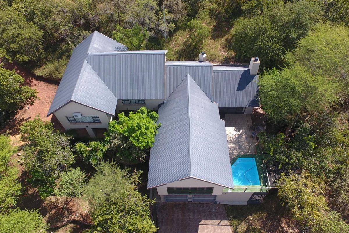 Aerial view of a residential property featuring a corrugated metal roof, a swimming pool, and surrounding mature trees.
