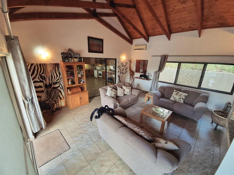 Spacious living room featuring a high vaulted ceiling with exposed timber rafters, tiled flooring, and large windows providing natural light.