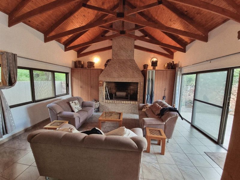 Spacious living room featuring a vaulted timber ceiling with exposed trusses, a central tiled fireplace, built-in cabinetry, and large sliding glass doors.