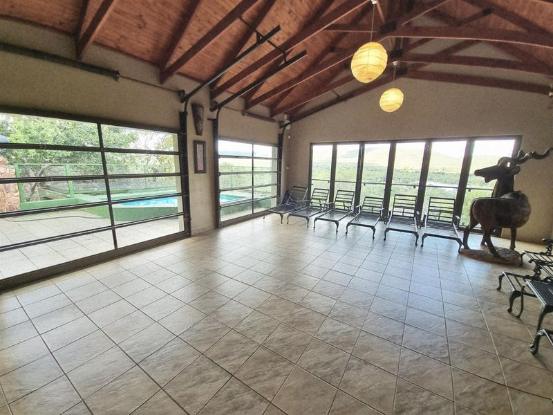 Spacious living area featuring exposed timber roof trusses, tiled flooring, and large glass doors providing expansive views and access to the outdoor pool area.