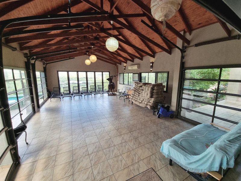 Spacious covered patio featuring exposed timber trusses, tiled flooring, and large glass doors providing seamless indoor-outdoor flow and expansive views.