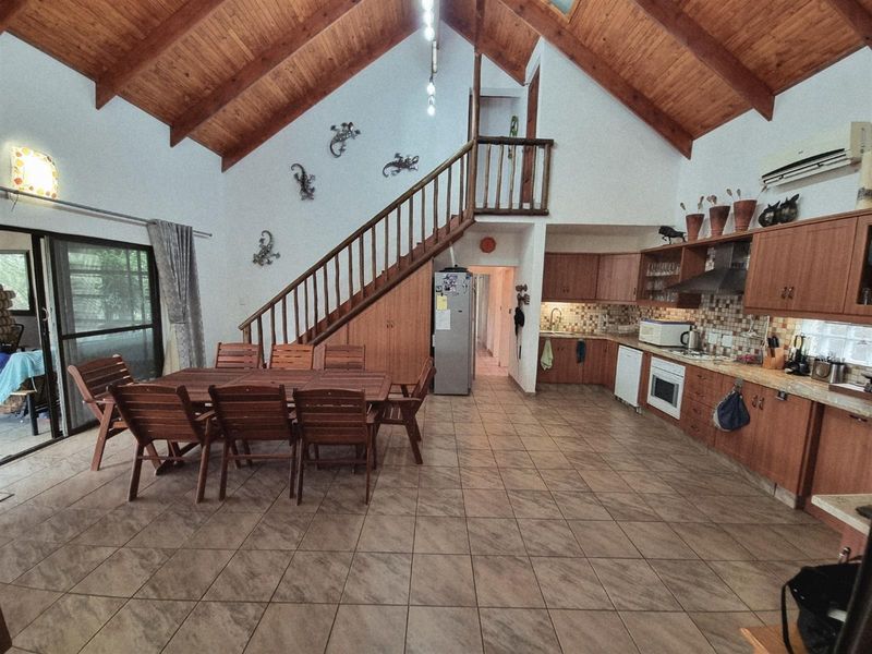 Spacious open-plan living and kitchen area featuring a high vaulted timber ceiling, tiled floors, and a wooden staircase leading to an upper level.