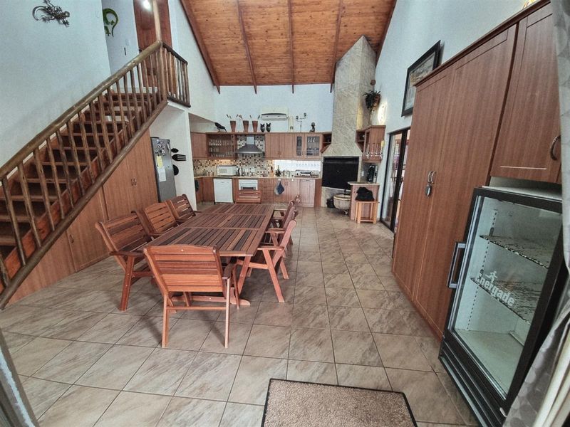 Spacious open-plan living and kitchen area featuring high exposed timber ceilings, a built-in fireplace, and a timber staircase.
