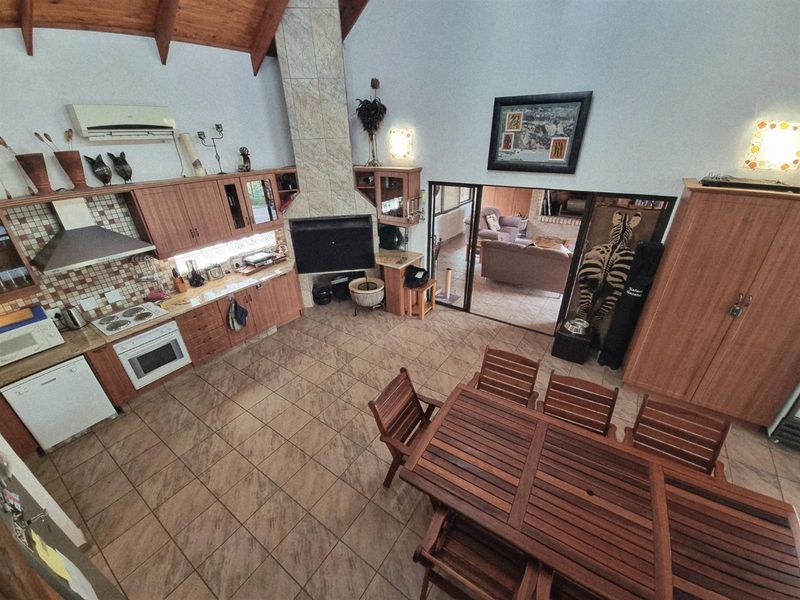 Spacious open-plan kitchen and dining area featuring a vaulted timber ceiling, tiled floors, and a central built-in fireplace with direct access to an adjacent room.