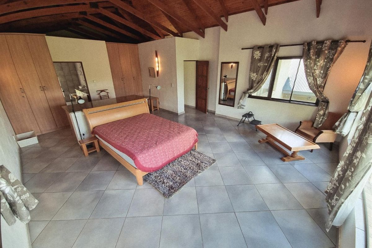 Spacious bedroom featuring a vaulted timber ceiling, tiled flooring, and extensive built-in cupboard storage with an integrated en-suite bathroom.