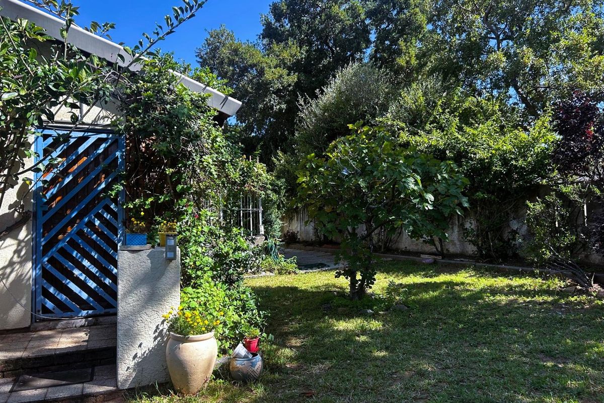 A private rear garden featuring established trees, a lawn area, and a paved walkway leading to the side of the house.