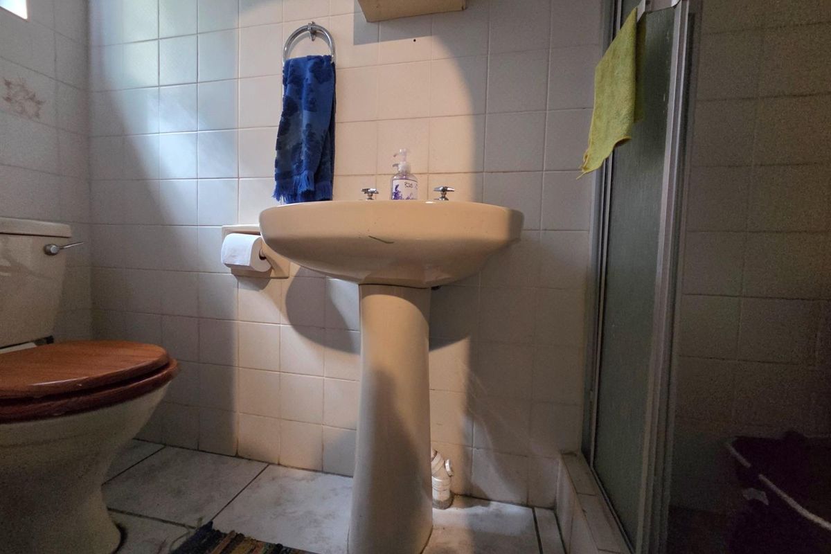 A dated bathroom featuring a pedestal basin, toilet, and shower enclosure with tiled finishes, requiring modernization to improve functionality and aesthetic appeal.