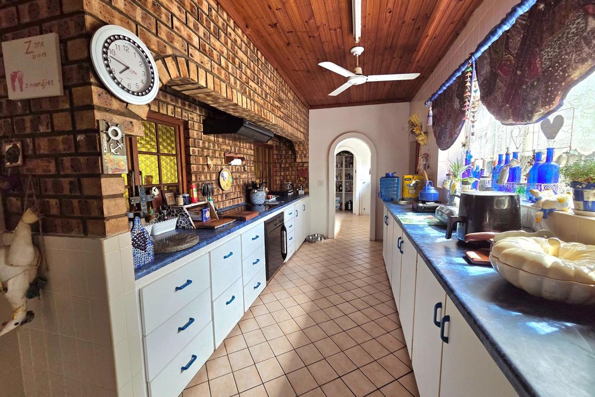A rustic kitchen featuring exposed brick walls, timber ceilings, tiled flooring, and extensive built-in cabinetry with a functional layout.