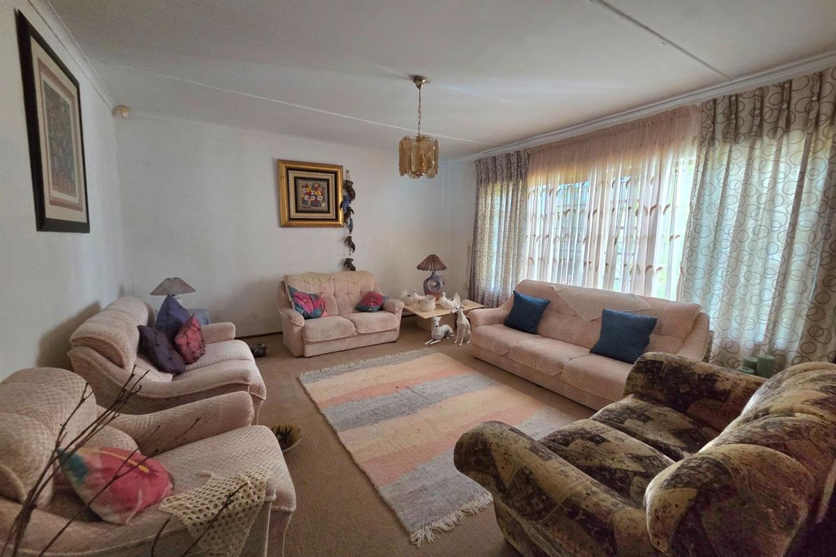 A spacious living room featuring neutral wall finishes, fitted carpeting, and large windows with established curtain tracks, offering a comfortable and functional living space.