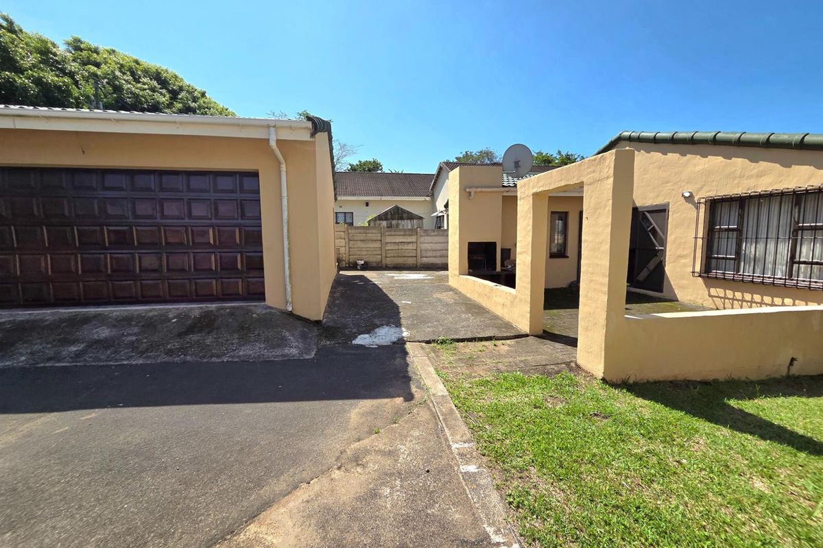 Rear exterior view featuring a garage, paved driveway, and a covered patio area with a built-in braai.