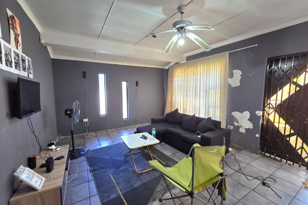 Living room featuring tiled flooring, a ceiling fan, and security gate access. The walls require maintenance and repainting.