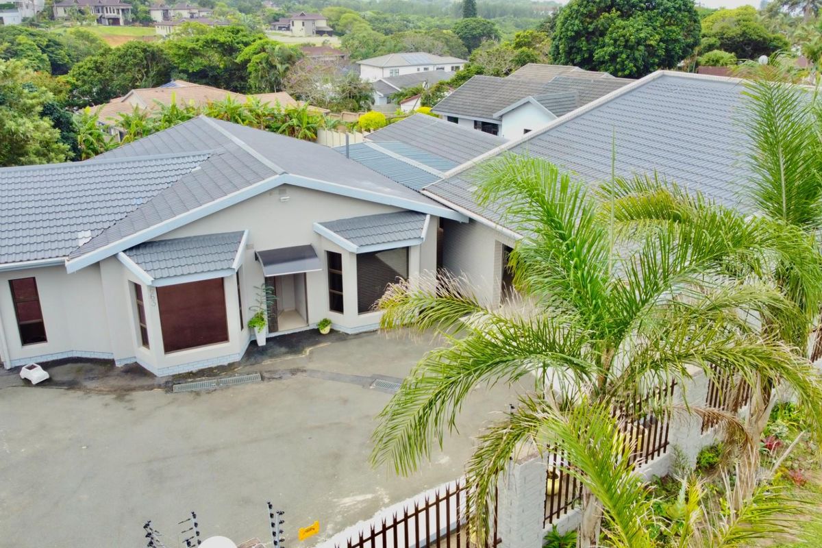 Aerial view of a modern residential property featuring a tiled roof, paved driveway, and secure perimeter fencing in a suburban setting.