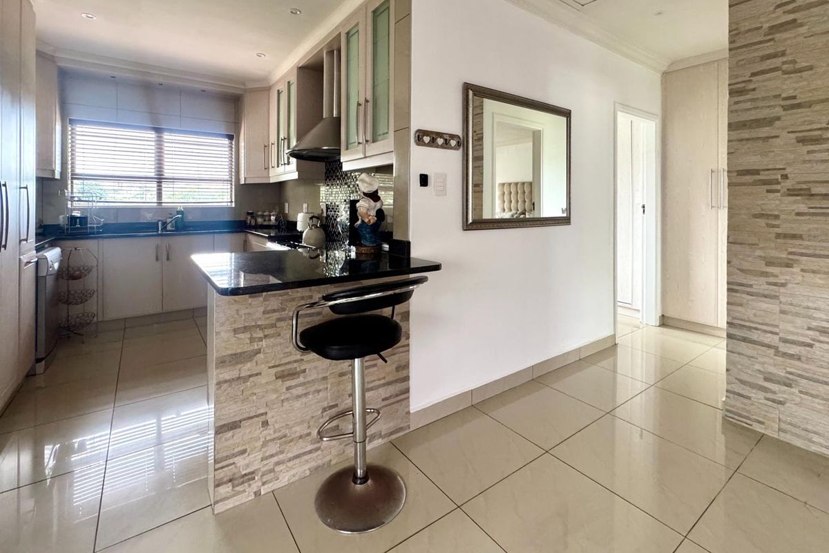 A modern kitchen featuring granite countertops, a breakfast bar with stone cladding, built-in cabinetry, and tiled flooring throughout the open-plan living space.