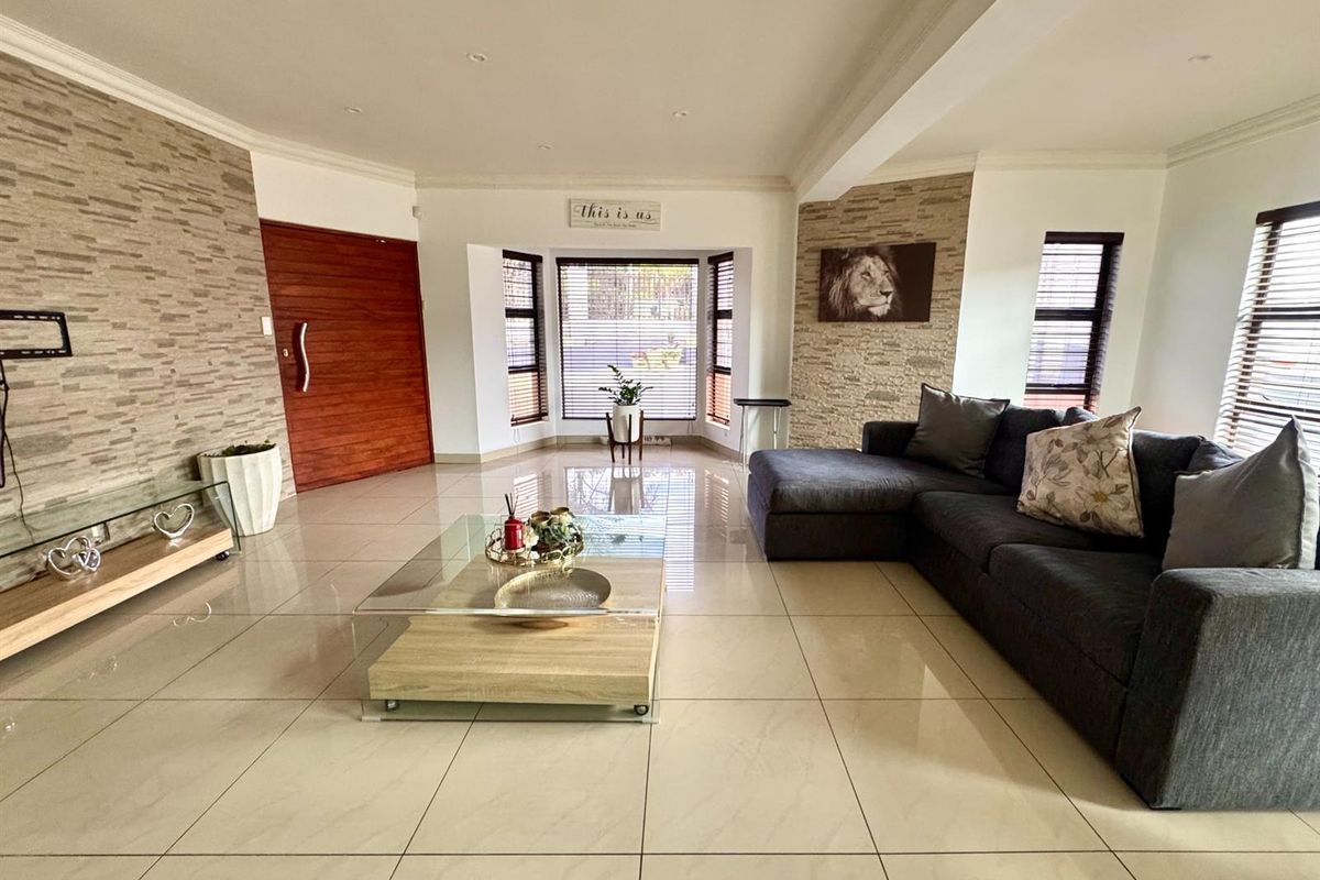 Spacious living room featuring large format floor tiles, stone-cladding feature walls, recessed downlighting, and a solid timber entrance door.
