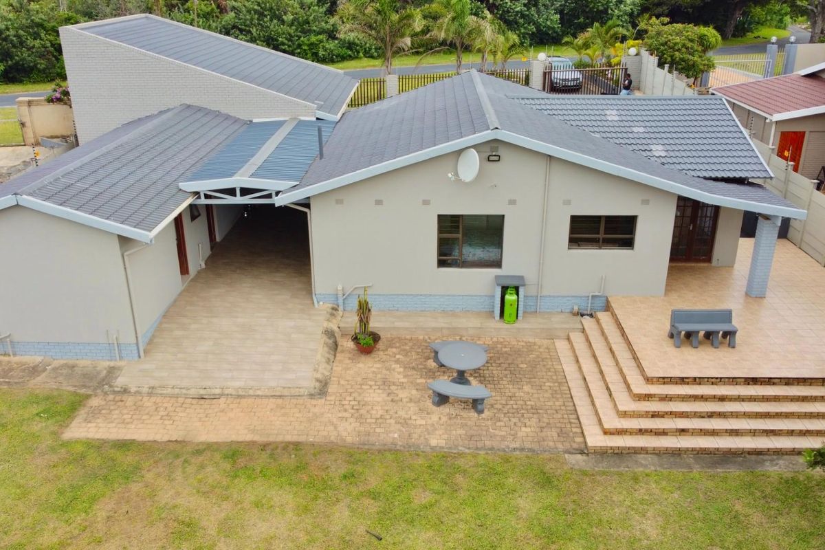 Aerial view of the rear exterior featuring a tiled patio, covered carport area, paved courtyard, and a well-maintained tiled roof.
