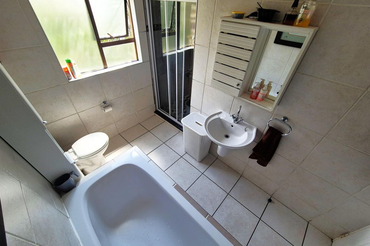 A functional bathroom featuring a bathtub, separate shower enclosure, wall-mounted basin, and toilet with tiled walls and flooring.