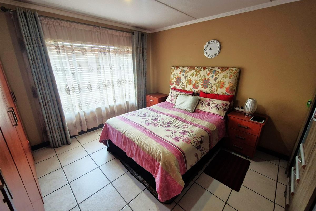 A functional bedroom featuring tiled flooring, large window with fitted blinds, and neutral wall tones, providing a comfortable and practical living space.