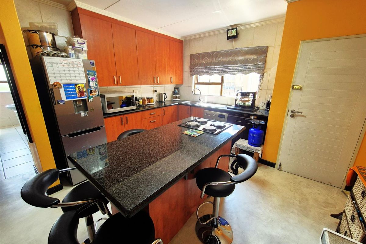 A functional kitchen featuring wooden cabinetry, a central island with a dark granite countertop, integrated hob, and tiled splashbacks.