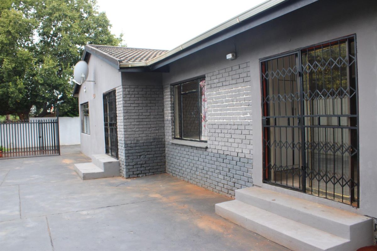Rear exterior view of the property featuring grey painted brickwork, concrete patio area, and security gates on sliding doors.