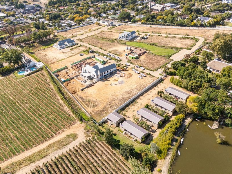 Aerial view of a residential development site featuring ongoing construction, surrounding vineyards, and proximity to a lake.