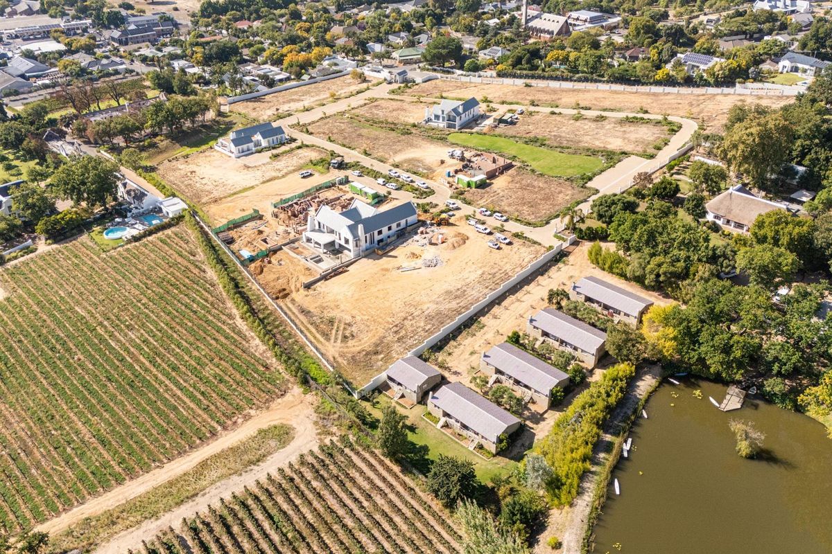 Aerial view of a residential development site featuring ongoing construction, surrounding vineyards, and proximity to a lake.