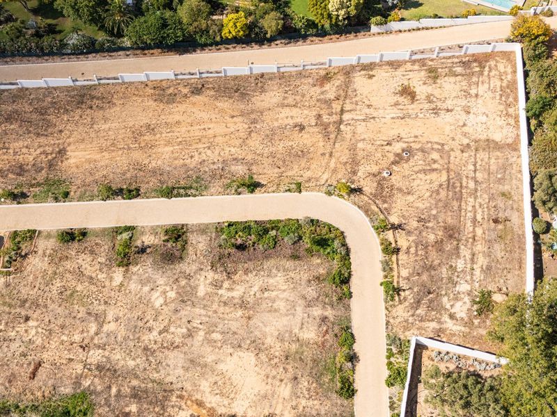 Aerial view of a vacant residential plot featuring a paved driveway and perimeter boundary walls, ready for development.