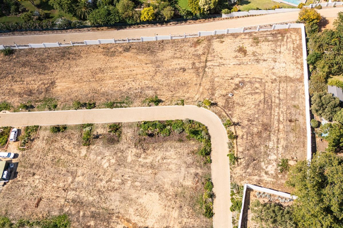 Aerial view of a vacant residential plot featuring a paved driveway and perimeter boundary walls, ready for development.