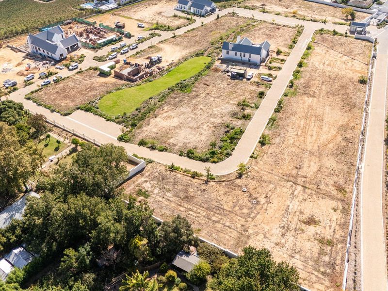 Aerial view of a residential development site featuring cleared land, paved access roads, and surrounding established properties.