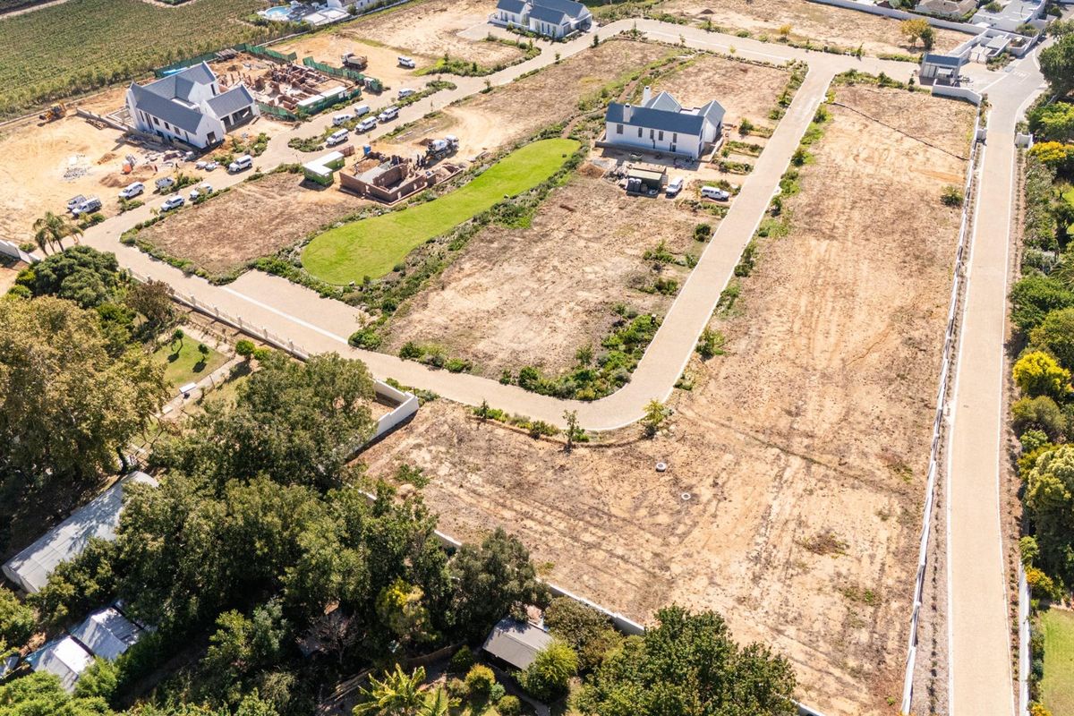Aerial view of a residential development site featuring cleared land, paved access roads, and surrounding established properties.