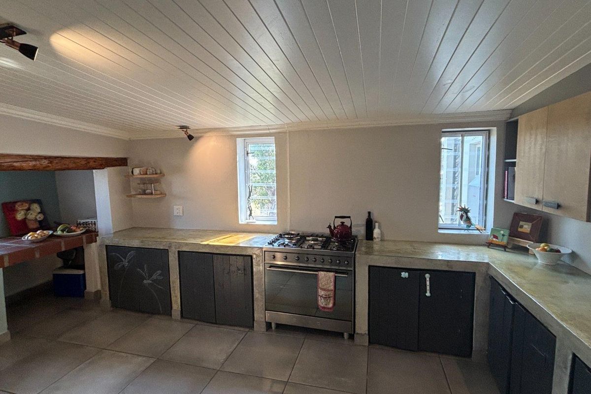 Rustic farmhouse kitchen featuring concrete countertops, custom cabinetry, a gas range, and a white tongue-and-groove ceiling.
