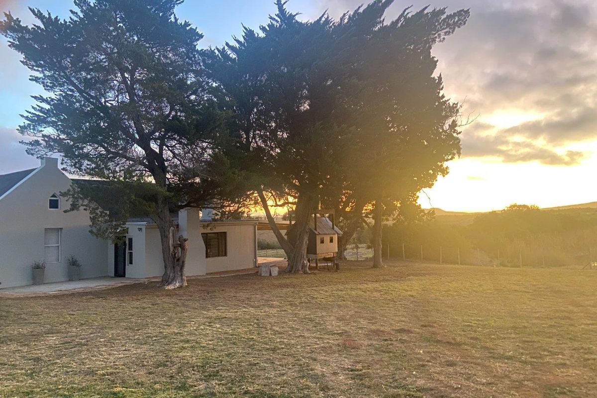 A scenic view of the farm property exterior at sunset, featuring mature trees, open grounds, and the side elevation of the main dwelling.