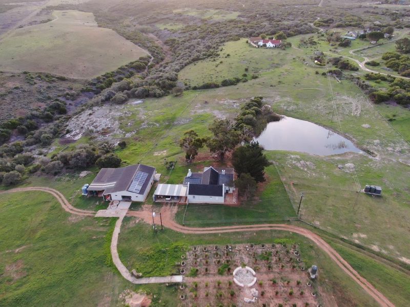 Aerial view of a farm property featuring a main residence, outbuildings, solar panels, a private dam, and established garden areas.