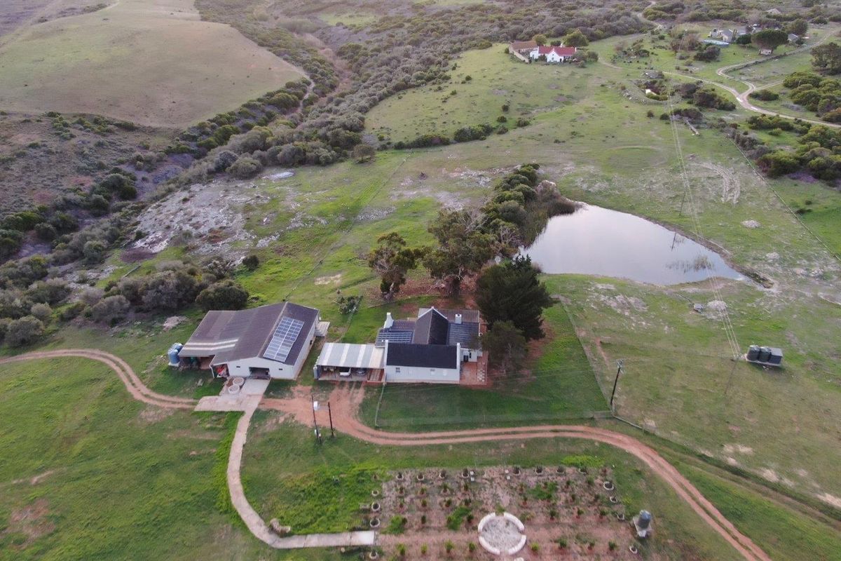 Aerial view of a farm property featuring a main residence, outbuildings, solar panels, a private dam, and established garden areas.