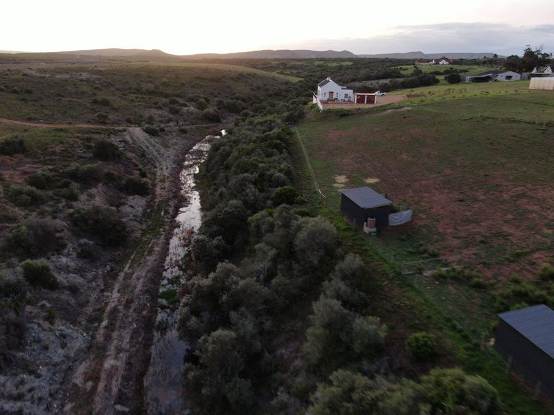 Aerial view of the farm property featuring a main residence, outbuildings, and a natural stream running through the landscape.