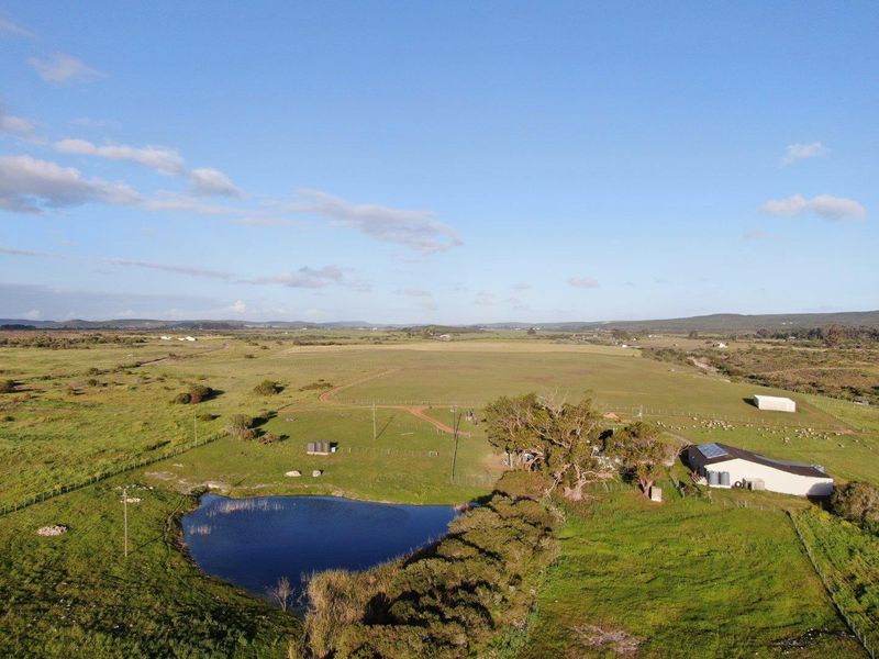 Aerial view of the expansive farm property featuring open grazing land, a natural dam, and existing farm outbuildings.
